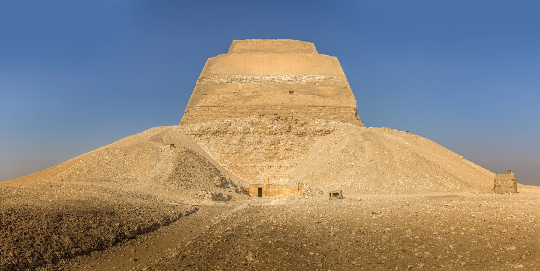 The Meidum pyramid: a bare three-stage stone tower rising out of a huge mound of its own collapsed casing, under a clear blue sky